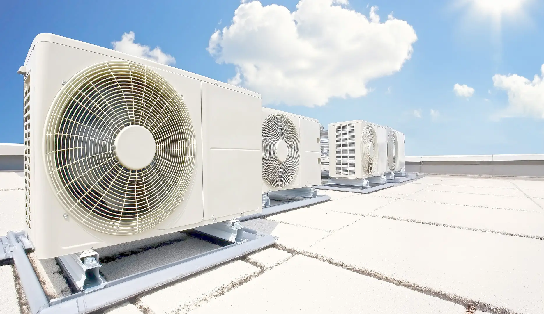Central air conditioning units installed on a rooftop under a bright blue sky with fluffy clouds.