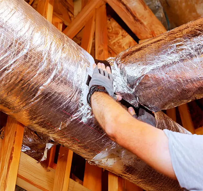 Contractor worker adjusts insulation around ductwork in residential attic, ensuring proper sealing efficiency.