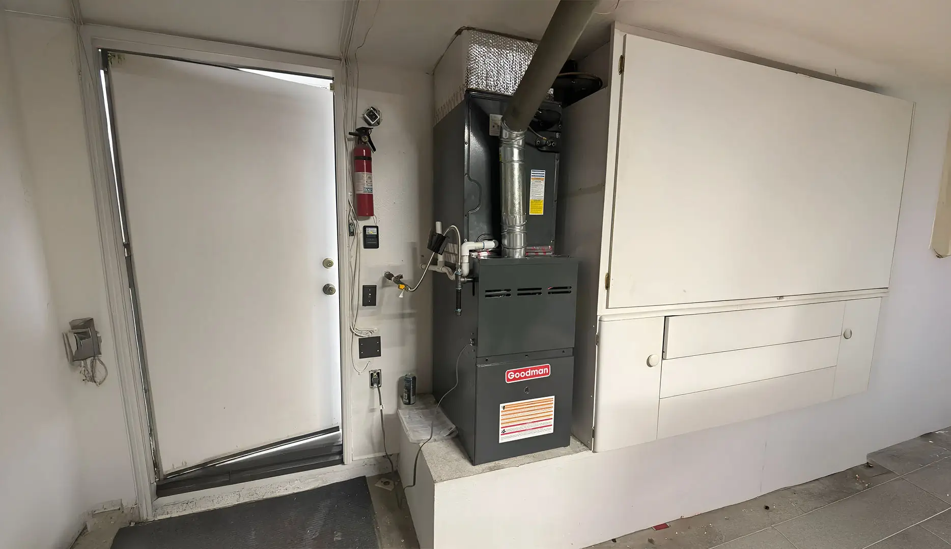Heater in a basement, to the left is a semi open door and to the right are some cabinets.