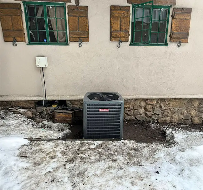 A lone AC unit outside a home with snow on the ground.
