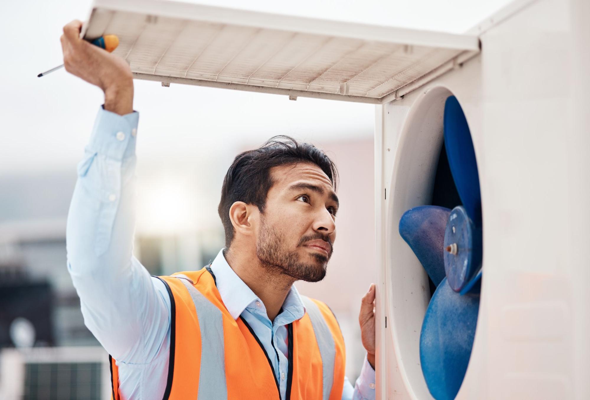 An HVAC technician examines the interior components of an AC condenser unit with a tool in hand