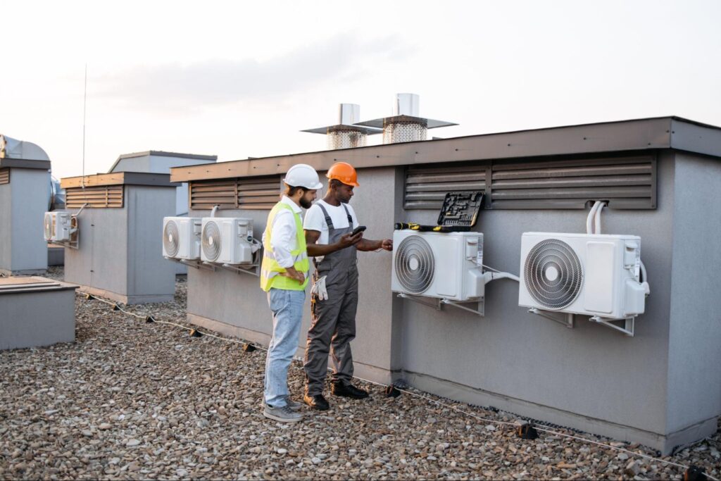 Two workers perform HVAC installation service while on top of a high building.