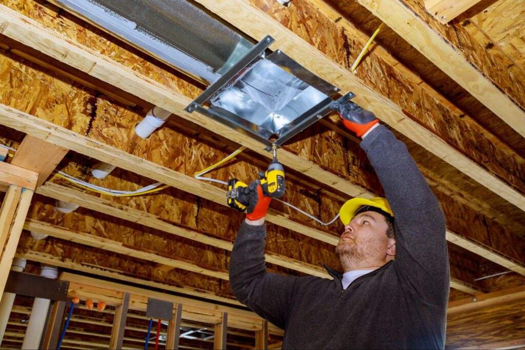 A technician mounts a heating and cooling system inside a home’s ceiling.