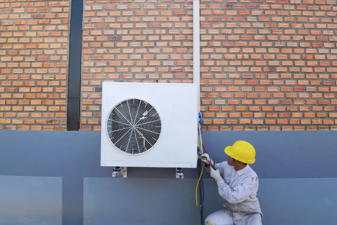 A technician installs an air conditioning unit outside a brick building.